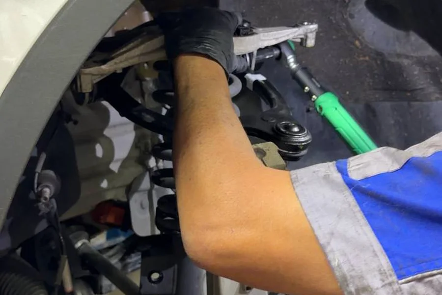 Mechanic replacing EV suspension bushing on control arm with red brake caliper visible EV Central SF