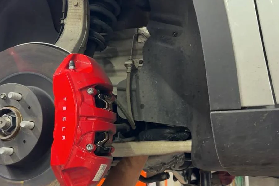 Mechanic replacing Tesla ball joint on lift with red Tesla brake caliper at EV Central Service San Francisco