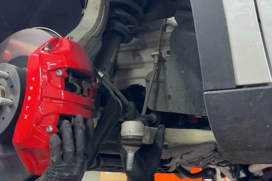 Mechanic replacing Tesla front control arm with red Tesla brake caliper visible at EV Central Service San Francisco